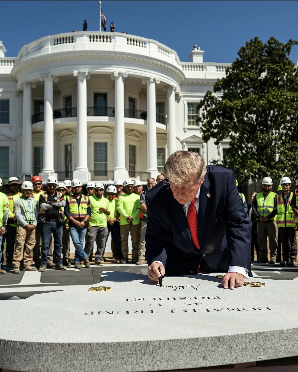 President Trump signs a granite cornerstone outside the White House as construction workers look on.